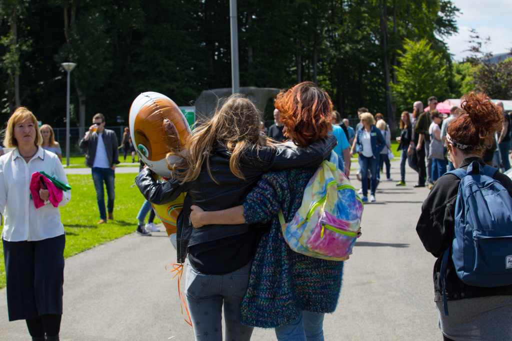 Foto van twee meiden die weglopen van de camera. Ze hebben een arm om elkaar heen. Eentje draagt een rugzak en de andere een grote ballon in de vorm van een dier. 