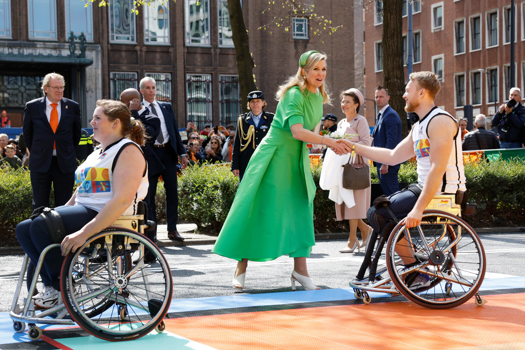 Foto van koningin Maxima die een hand geeft aan een basketbal speler in een rolstoel.  