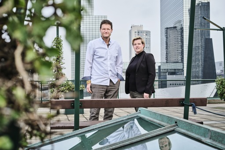 Foto van een man en een vrouw met op de achtergrond een aantal hogen gebouwen.