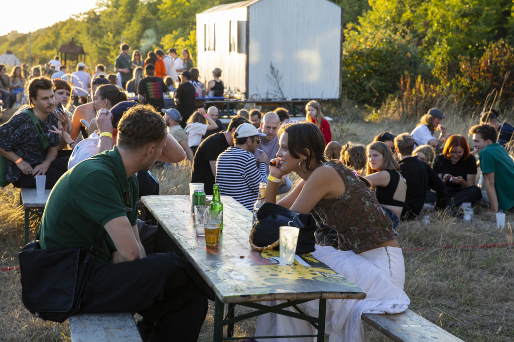 Foto van mensen die aan een picknick tafel zitten. Ze kijken elkaar aan en op de tafel staan een aantal drankjes. 