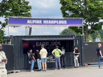 Foto van een Alpine oordoppen kraampje op een festival. Er staan een aantal personen voor die oordoppen aan het kopen zijn.